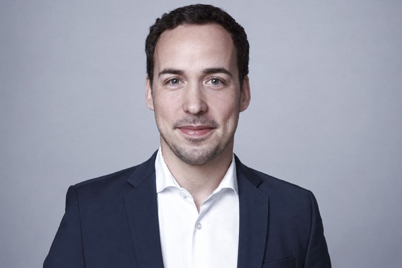 Florenz Klasen von TechMinds: Porträt im dunkelblauen Sakko mit weißem Hemd vor grauem Hintergrund.