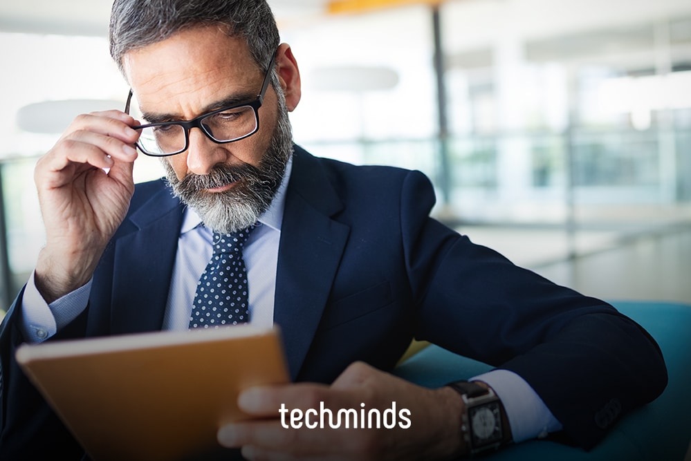Geschäftsführer im Anzug prüft Unterlagen am Tablet, Jobprofil Technischer Geschäftsführer