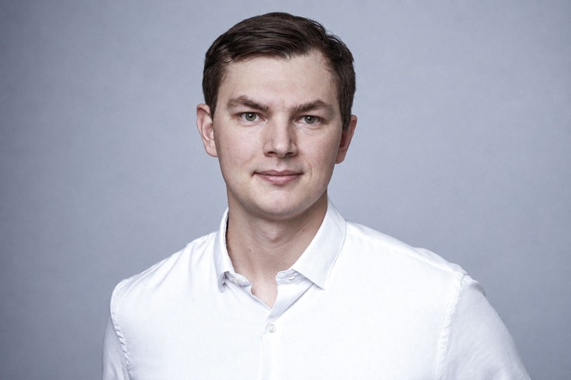 Bennet Schumacher von TechMinds im weißen Hemd, professionelles Porträt vor grauem Hintergrund.