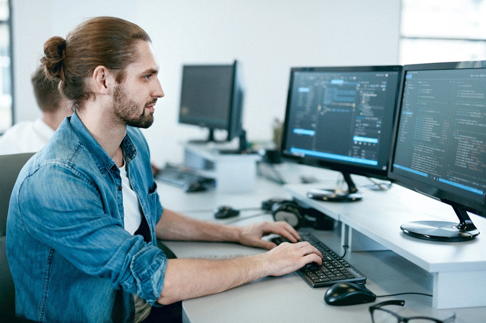 Softwareentwickler arbeitet an mehreren Monitoren mit Quellcode