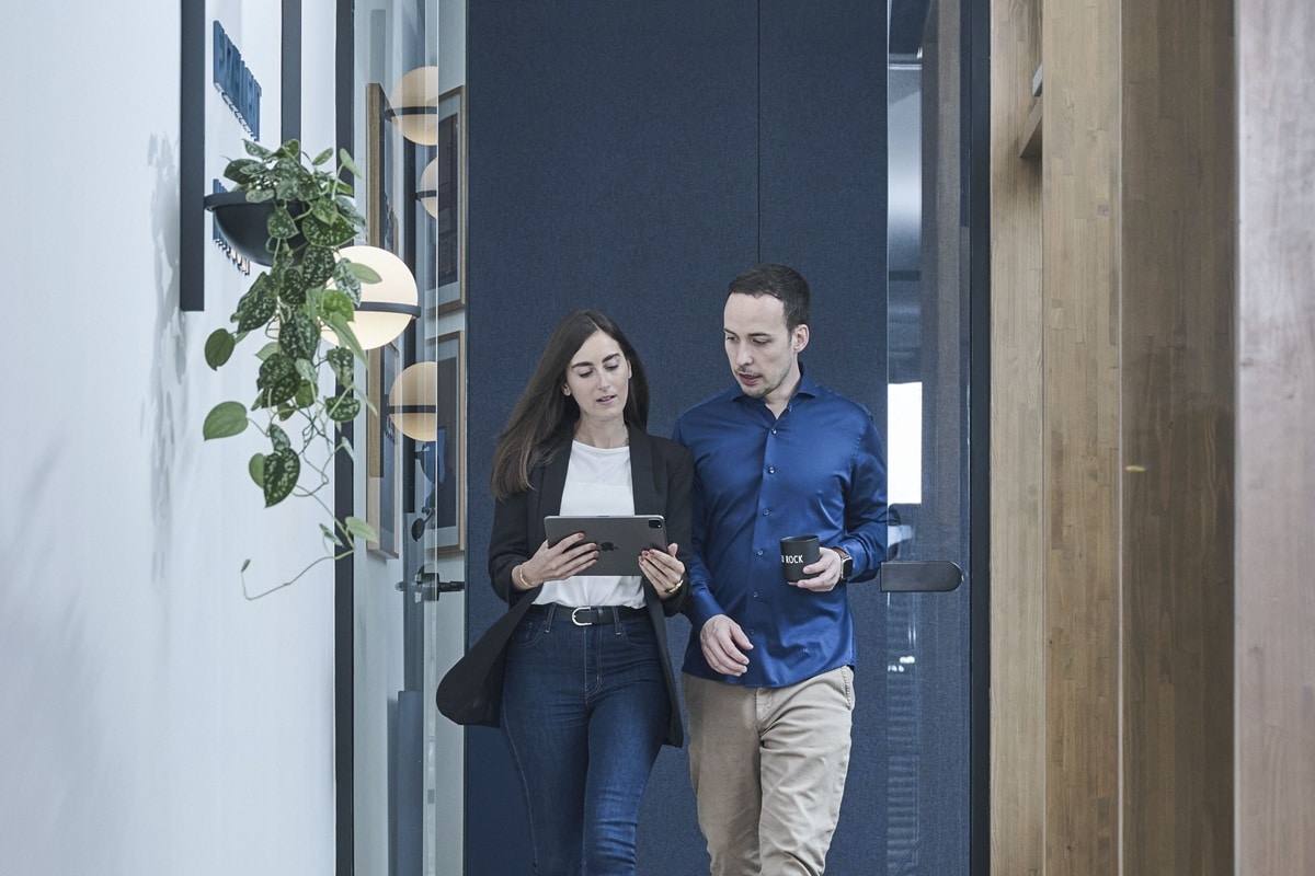 Zwei TechMinds-Kollegen besprechen Daten auf einem Tablet im modernen Büroflur.