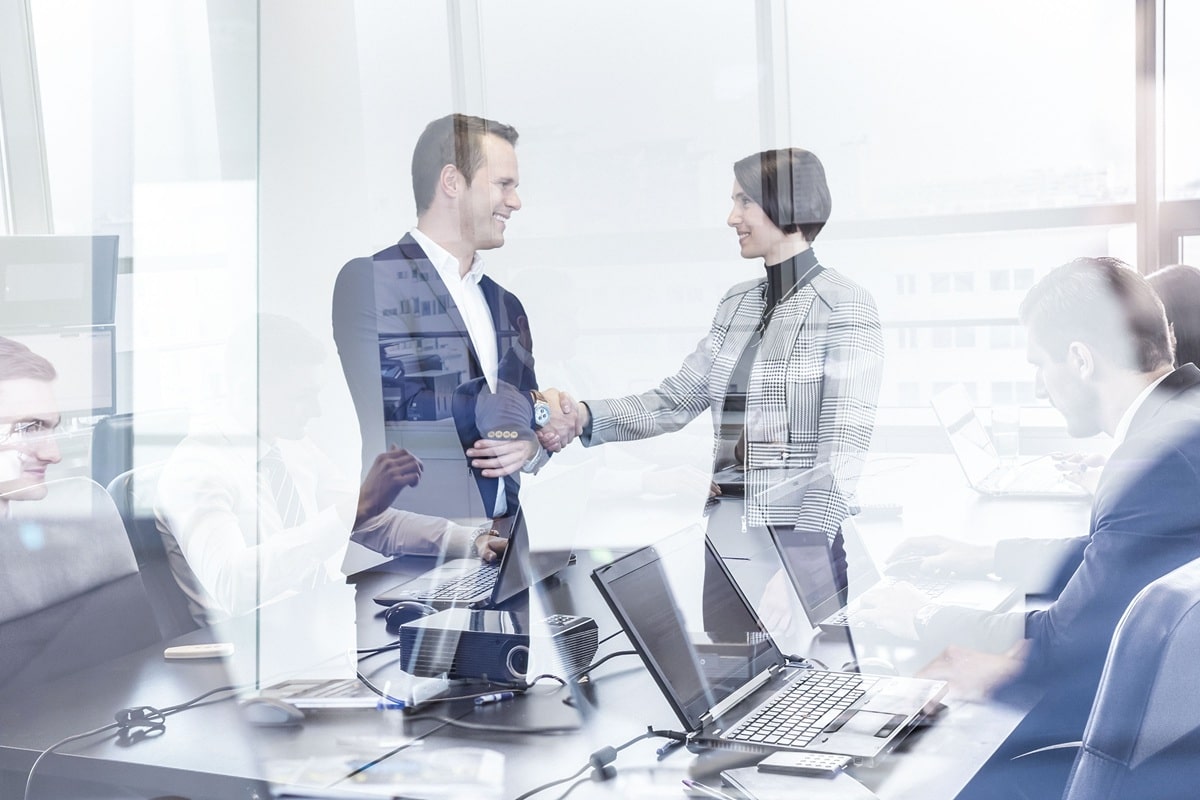 Zwei Männer im Anzug geben sich im Büro die Hand