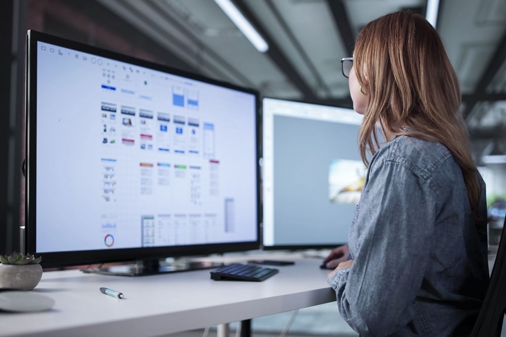 Designerin arbeitet an zwei Monitoren mit Benutzeroberflächen