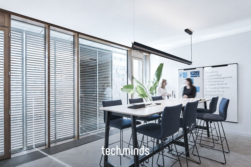 Meetingraum mit Hochtisch im TechMinds Büro Hamburg, zwei Mitarbeitende am Whiteboard