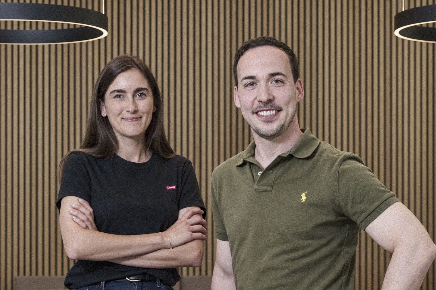 Warum TechMinds: Zwei Teammitglieder lächeln im modernen Büro vor Holzwand – Team von TechMinds.